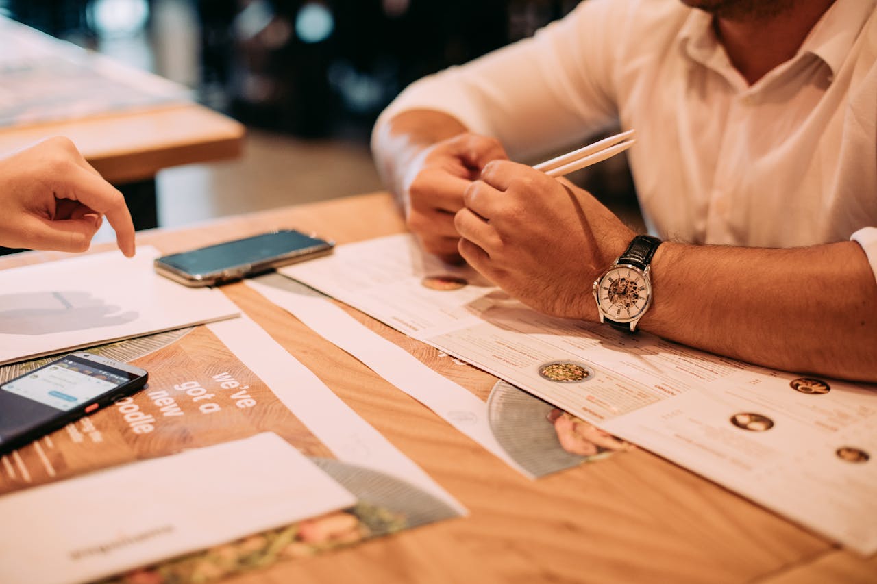 Home Two adults discussing a menu at a restaurant table with chopsticks and phones.
